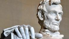 A closeup of the Lincoln Memorial in Washington, DC showing just the president's face and right hand chiseled from stone.