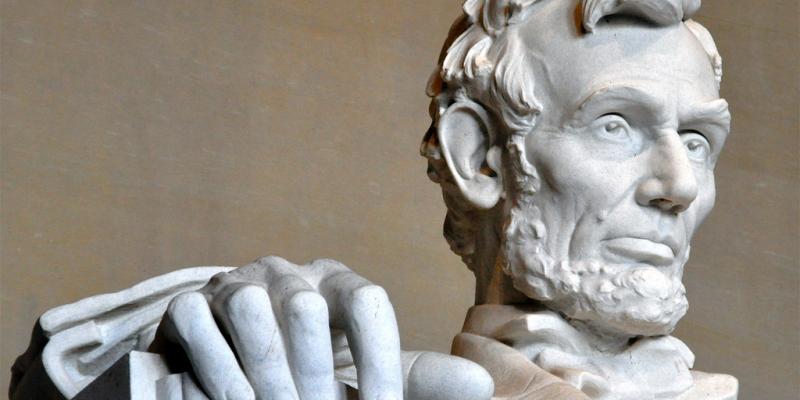 A closeup of the Lincoln Memorial in Washington, DC showing just the president's face and right hand chiseled from stone.