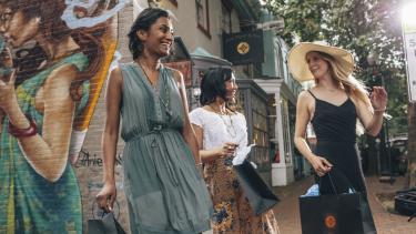 Three women with shopping bags in front of a mural