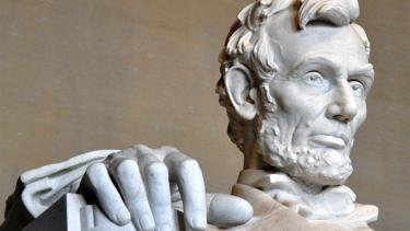 A closeup of the Lincoln Memorial in Washington, DC showing just the president's face and right hand chiseled from stone.